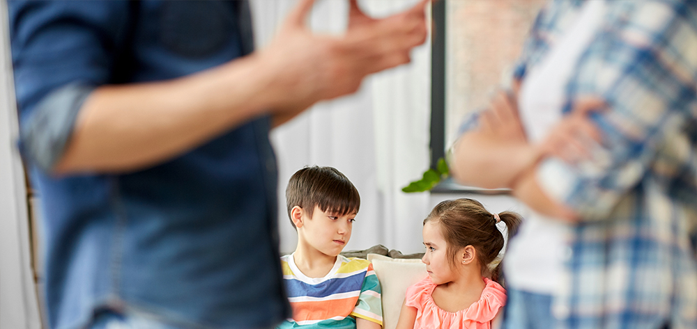 Image of an ex or married couple in the foreground, blurred, showing a discussion with children in focus in the background not looking very happy